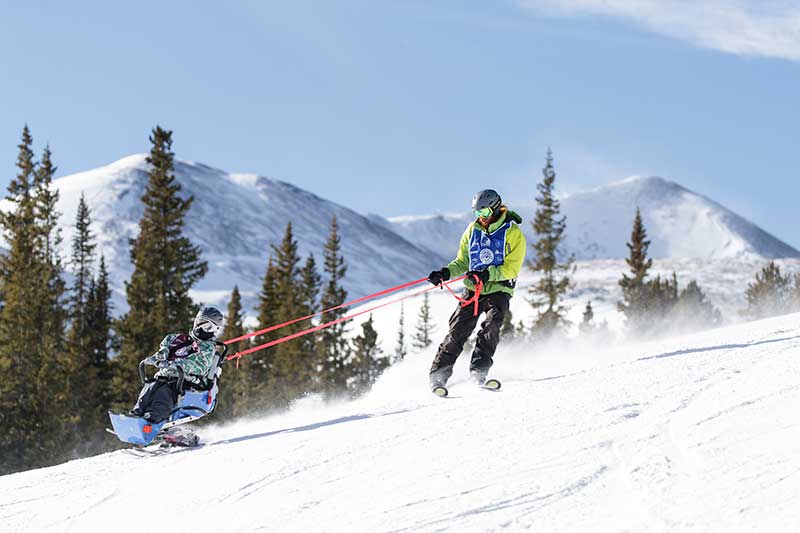 BOEC Ski Instructor Nick Melotte tethers an adaptive ski participant